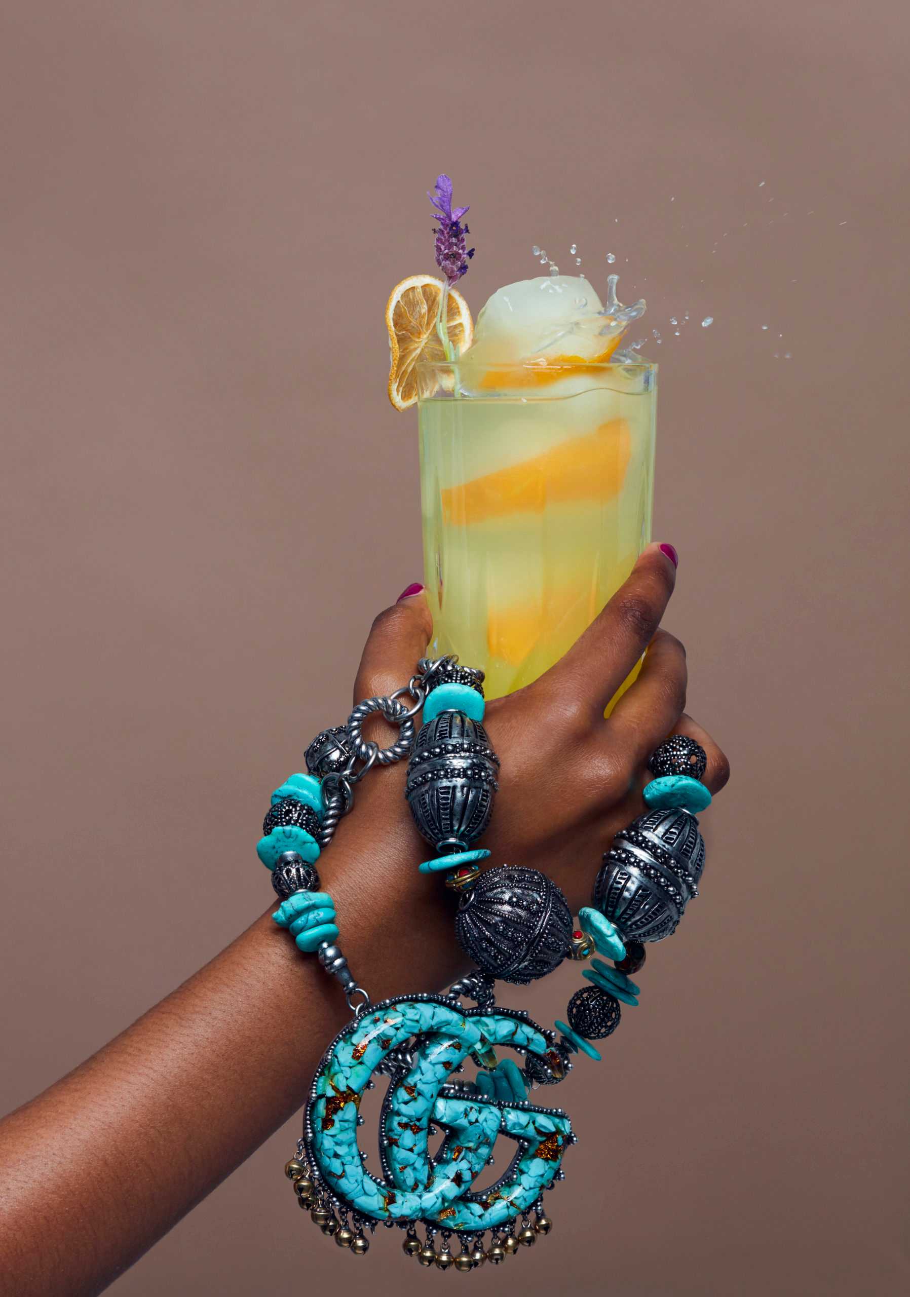 hands holding cocktail and turquoise gucci jewlery